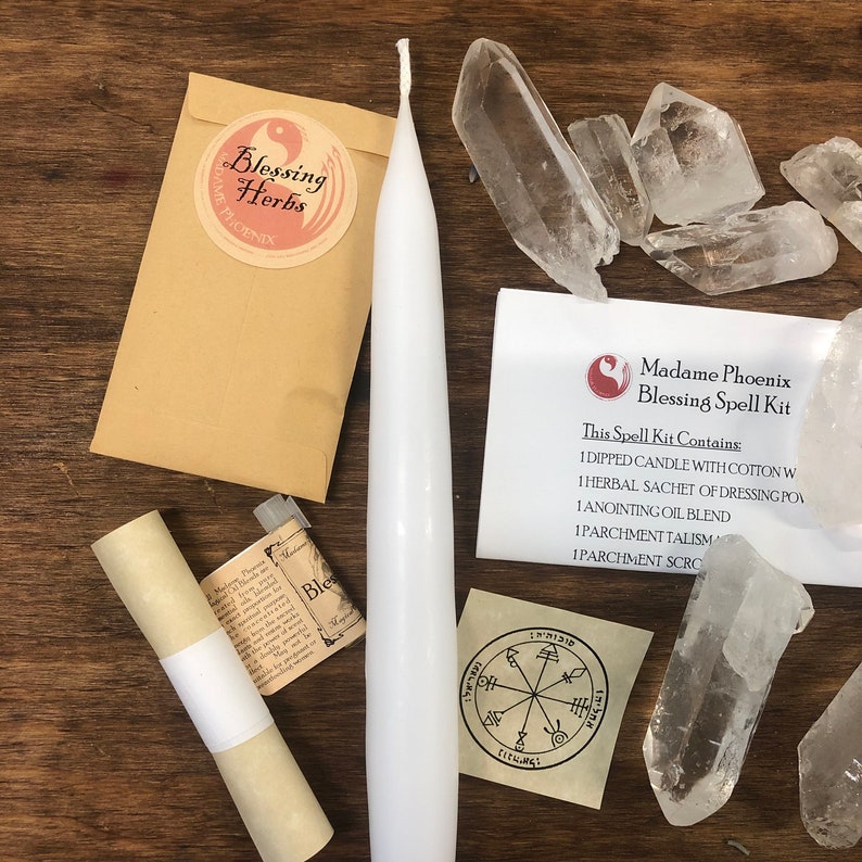 May include: A white candle, a brown envelope with a sticker that says "Blessing Herbs", a small bottle of oil, a rolled up parchment, a small piece of parchment with a sigil, and several clear quartz crystals. The text on the white card says "Madame Phoenix Blessing Spell Kit. This Spell Kit Contains: 1 Dipped Candle with Cotton Wick, 1 Herbal Sachet of Dressing Powder, 1 Anointing Oil Blend, 1 Parchment Talisman, 1 Parchment Scroll."