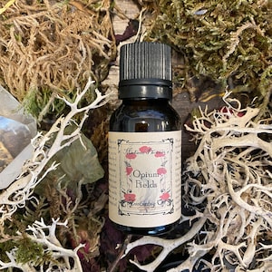 Könnte beinhalten: Eine kleine braune Glasflasche mit schwarzem Verschluss. Das Etikett lautet "Madame Phoenix's Opium Fields Anointing Oil".