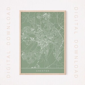 Puede incluir: Una impresión enmarcada del mapa de Chester, Inglaterra, en un estilo minimalista. El mapa presenta líneas blancas sobre un fondo verde apagado, con el nombre de la ciudad en la parte inferior. El marco es de color madera clara, con "DESCARGA DIGITAL" impreso verticalmente.