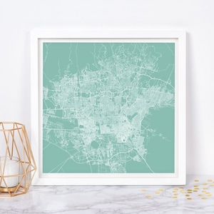 Pode incluir: Uma impressão emoldurada de um mapa da cidade com linhas brancas sobre um fundo azul-esverdeado. O mapa mostra as ruas e estradas de uma cidade.