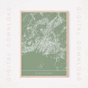 Puede incluir: Un mapa enmarcado de Hiroshima, Japón, en un estilo minimalista. El mapa presenta calles y topografía blancas detalladas sobre un fondo verde apagado. La palabra "Hiroshima" está impresa en blanco en la parte inferior del marco. Las palabras "DESCARGA DIGITAL" están impresas verticalmente.