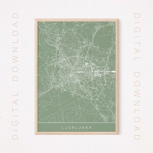 May include: A framed map print of Ljubljana, Slovenia, in a minimalist style. The map features white lines on a muted green background, with the city name at the bottom. The frame is a light wood color, and the words "DIGITAL DOWNLOAD" are printed vertically on the sides.