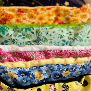 May include: A stack of colourful fabric squares with different patterns, including floral, butterfly, and chicken designs. The fabric squares are sewn together to create a layered effect.