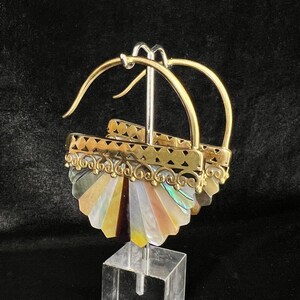 May include: A pair of gold hoop earrings with a fan-shaped design made of iridescent mother-of-pearl. The earrings are on a display stand.