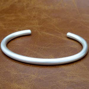 May include: A silver bangle bracelet with a smooth, rounded surface.
