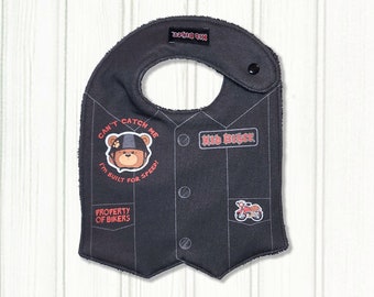 Könnte beinhalten: Schwarzes und graues Baby-Lätzchen mit einem Motorradwesten-Design. Es zeigt einen Comic-Bären mit Helm und dem Text "Can't Catch Me I'm Built For Speed!" und dem Text "Kid Biker" in Rot. Das Lätzchen hat auch den Text "Property of Bikers" und eine kleine Motorradgrafik.