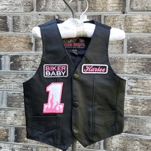 May include: Black leather vest with pink patches that say "Biker Baby", "Harlee", and "1" with a flame design. The vest has a Kid Biker Motorcycle Apparel label and size tag.