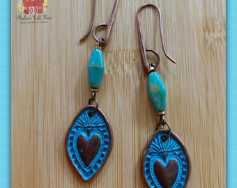 May include: A pair of handcrafted copper earrings with turquoise beads and a heart-shaped pendant. The pendant has a blue background with a copper heart in the center. The earrings are displayed on a wooden surface. The text "Marlene's Craft House" is visible.