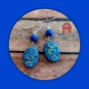 May include: Blue and green polymer clay earrings with a seashell design. The earrings are oval shaped and have a blue bead at the top of the earring.