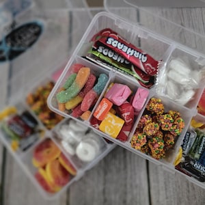 May include: Clear plastic organizer filled with various candies. The compartments hold colorful gummy worms, Airheads, wrapped candies, and ring-shaped gummies. A selection of other candies are also visible.