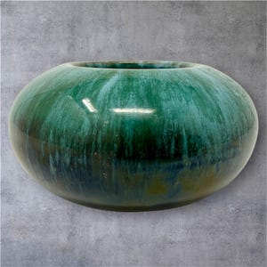 May include: A round, glazed ceramic vase in shades of teal and green. The vessel has a wide opening and a smooth, glossy finish. The color transitions from dark green at the base to lighter teal near the top, creating a gradient effect.
