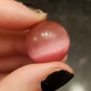 Puede incluir: Una cuenta de piedra de ojo de gato rosa y blanca.