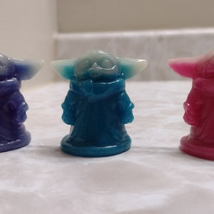 May include: Three small figurines of a popular character from the Star Wars franchise. The figurines are made of a translucent material and are painted in blue, pink, and purple.