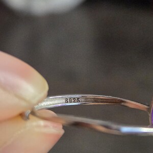 Puede incluir: Primer plano de un anillo de plata con la marca "S925" visible. El anillo est&aacute; sujeto por una persona. El anillo tiene un acabado pulido.