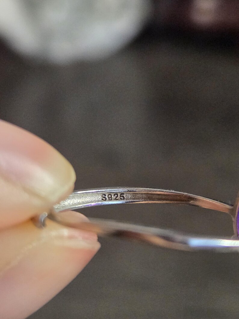 Puede incluir: Primer plano de un anillo de plata con la marca "S925" visible. El anillo est&aacute; sujeto por una persona. El anillo tiene un acabado pulido.