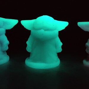 May include: Three glow-in-the-dark figurines of a popular character from the Star Wars franchise. The figurines are in different shades of blue and pink.