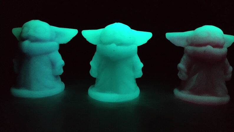 May include: Three glow-in-the-dark figurines of a popular character from the Star Wars franchise. The figurines are in different shades of blue and pink.