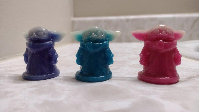 May include: Three small figurines of a popular character from the Star Wars franchise. The figurines are made of a translucent material and are painted in blue, pink, and purple.