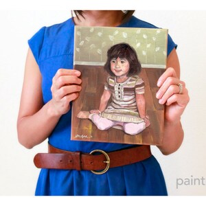 May include: A painting of a young girl sitting on a wooden floor. She is wearing a striped shirt and a pink skirt. The painting has a light brown background with a pattern of white leaves.