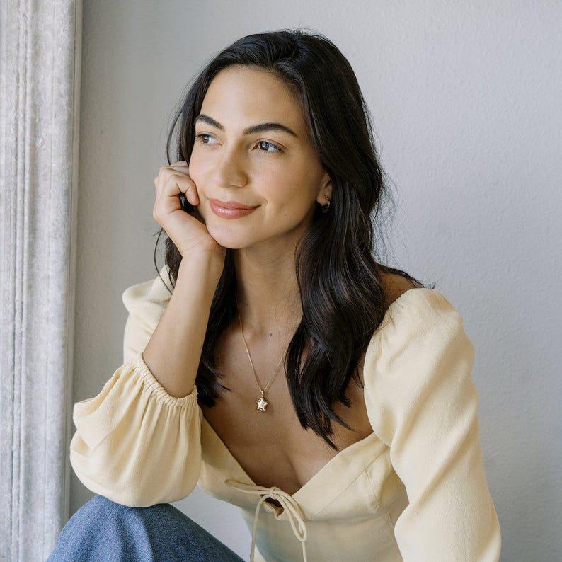 Woman wearing a Polly Star Locket Necklace, styled with a soft yellow top, showcasing a charming star locket design.