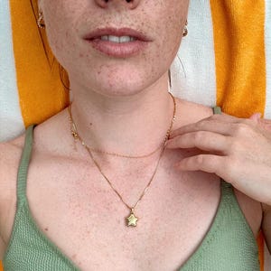 Close-up of a woman wearing a Polly Star Locket Necklace on a sunny background, showcasing the charming star design.