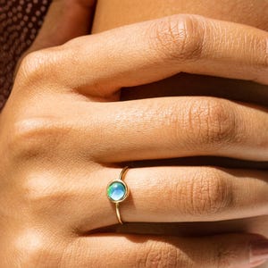 May include: A silver ring with a round, amber-colored stone. The ring's band is thin and smooth, and the stone is set in a bezel setting. The ring is displayed on a clear glass surface.