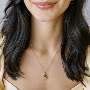 Close-up of a woman wearing a Polly Star Locket Necklace over a cream top, showcasing its charming star design.