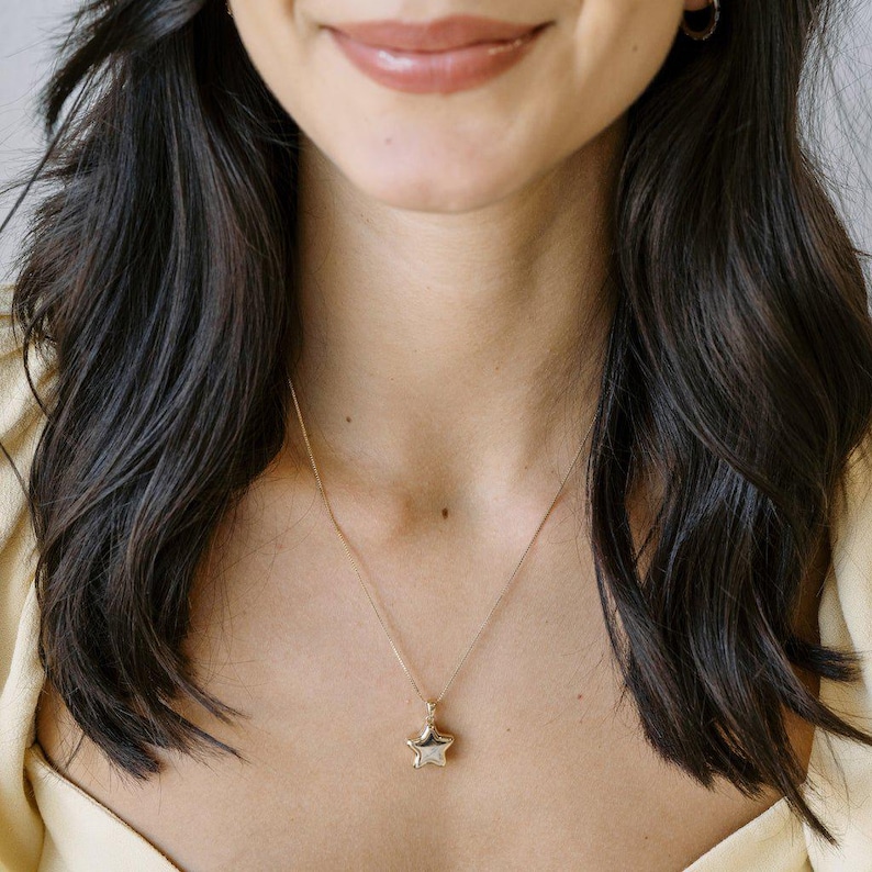Close-up of a woman wearing a Polly Star Locket Necklace over a cream top, showcasing its charming star design.