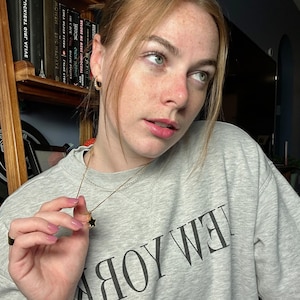 Model wearing a Polly Star Locket Necklace, showcasing its unique charm against a cozy backdrop.