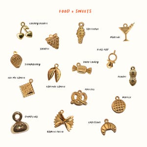 May include: A collection of gold-toned metal charms featuring food and sweets themes, including shapes like cherry hearts, grapes, soft serve, martini, strawberry, hard candy, ring pop, peanut, eat me cookie, fortune cookie, pretzel, waffle, dumpling, bowtie pasta, and croissant.