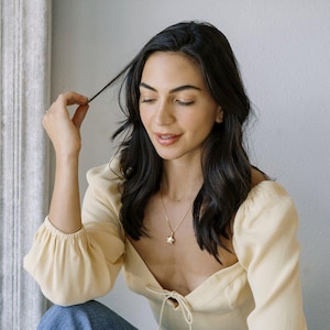 Woman in a yellow top wearing the Polly Star Locket Necklace, showcasing its charm and layered styling.