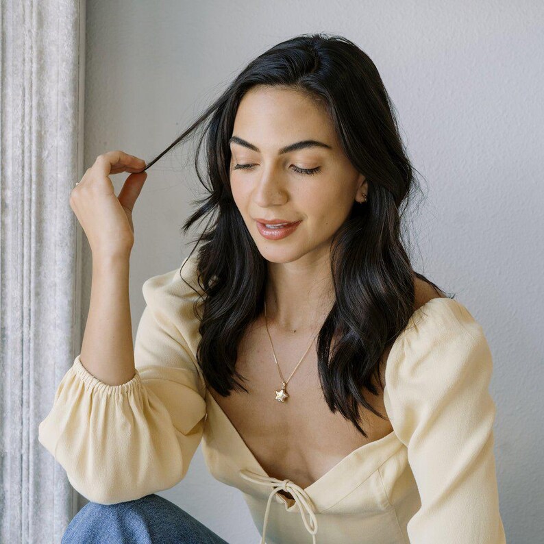 Woman in a yellow top wearing the Polly Star Locket Necklace, showcasing its charm and layered styling.