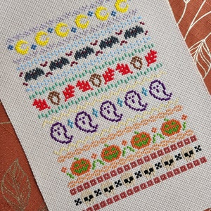 Peut inclure: Un motif de point de croix sur le th&egrave;me d'Halloween. Le motif pr&eacute;sente une vari&eacute;t&eacute; de symboles d'Halloween, notamment des fant&ocirc;mes, des citrouilles, des chauves-souris et des lunes. Le motif est brod&eacute; dans une vari&eacute;t&eacute; de couleurs, notamment l'orange, le noir, le blanc et le jaune.