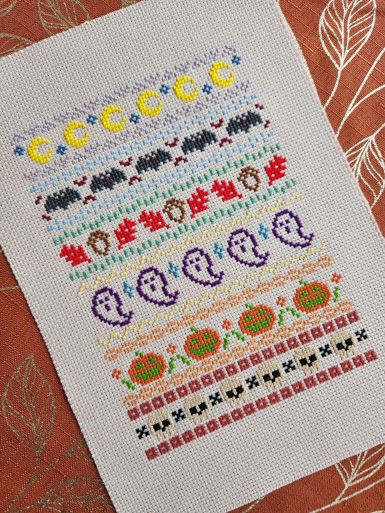 Peut inclure: Un motif de point de croix sur le th&egrave;me d'Halloween. Le motif pr&eacute;sente une vari&eacute;t&eacute; de symboles d'Halloween, notamment des fant&ocirc;mes, des citrouilles, des chauves-souris et des lunes. Le motif est brod&eacute; dans une vari&eacute;t&eacute; de couleurs, notamment l'orange, le noir, le blanc et le jaune.