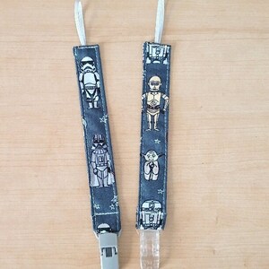 May include: Two blue and white fabric baby teethers with Star Wars characters. The teethers have a white clip and a white loop at the top. The characters on the teethers include Darth Vader, Yoda, R2-D2, C-3PO, and a Stormtrooper.