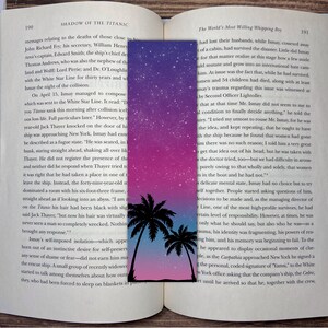 May include: A bookmark with a gradient background of pink and blue with white stars. Two palm trees are silhouetted against the sky. The bookmark has the text "The World's Most Willing Whipping Boy" at the top.