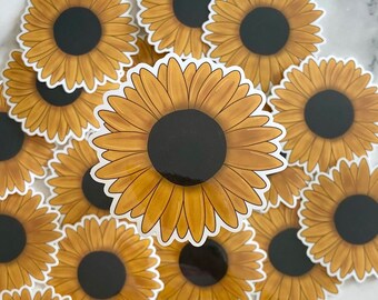 May include: A collection of yellow sunflower stickers with black centers. The stickers are arranged in a circular pattern on a white surface.