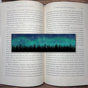 May include: A bookmark featuring a dark forest silhouette against a blue night sky with a shooting star and white stars. The bookmark is a great way to mark your place in a book.