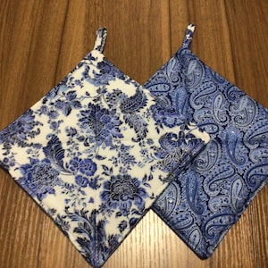 May include: Two blue and white patterned pot holders with a loop handle. One pot holder has a paisley design and the other has a floral design.