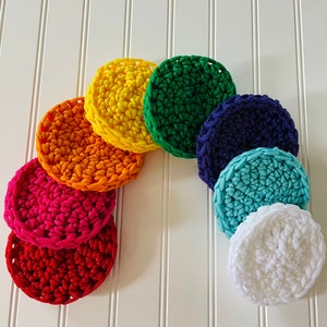 May include: A set of seven crocheted round pads in rainbow colors, including red, orange, yellow, green, blue, turquoise, and white.