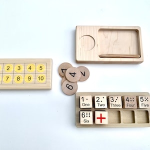 May include: Wooden tray with a set of number tiles. The tiles are numbered 1 through 10 and are arranged in a grid. There are also individual wooden circles with numbers 1 through 6. The tray has a small compartment for a pencil.