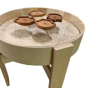 May include: A round wooden table with four legs and a glass top. The table has a decorative design on the top and four wooden coasters with Japanese characters on them.
