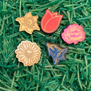 May include: Five wooden flower shapes in different colors and styles. The flowers are on a green background.