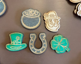 Op de afbeelding: Een verzameling houten uitsnijdingen met een St. Patrick's Day-thema. De uitsnijdingen omvatten een pot goud, een hoefijzer, een klavertjevier en een kabouter.