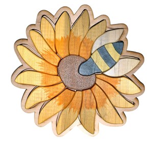 May include: Wooden sunflower puzzle with a bee. The sunflower has yellow and orange petals, a brown center, and a blue and yellow striped bee. The puzzle is made of wood and has a natural finish.