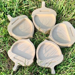 May include: Five wooden acorn-shaped trinket dishes with a small groove for holding a phone or other small items. The dishes are arranged in a circle on a bed of green grass.