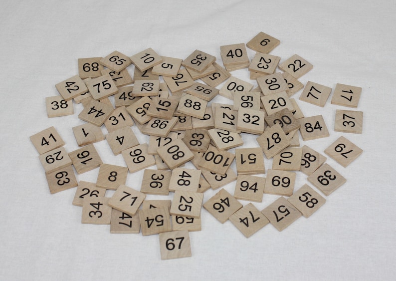 May include: A pile of wooden tiles with numbers printed on them. The tiles are scattered on a white surface.