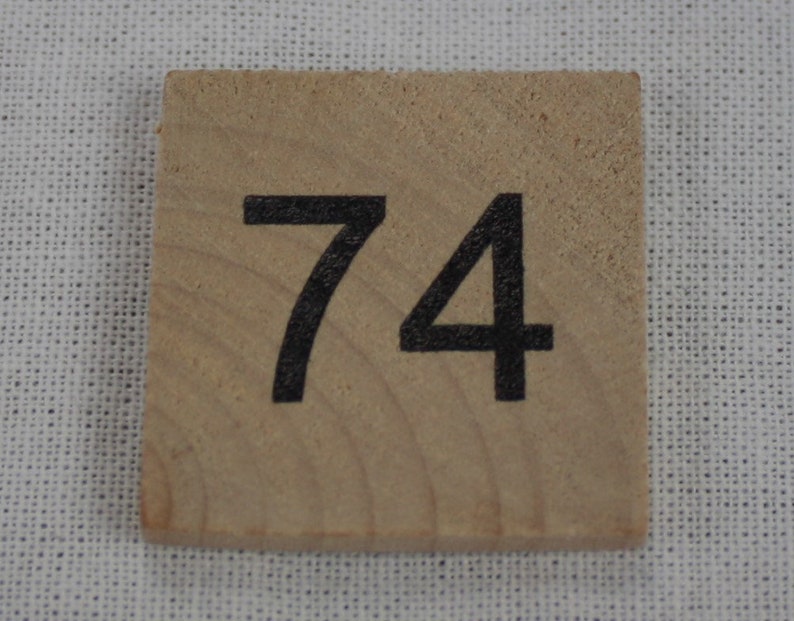 May include: A wooden tile with the number 74 printed in black.