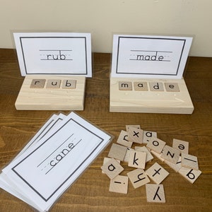 May include: A set of wooden letter tiles for spelling words, with a card holder for displaying the word "cane". The tiles are arranged to spell the words "rub" and "made".