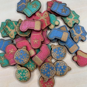 May include: A collection of wooden Christmas ornaments and decorations in various colors, including red, green, blue, and pink. The ornaments are shaped like mittens, ornaments, and gift boxes. Each ornament has a snowflake design.
